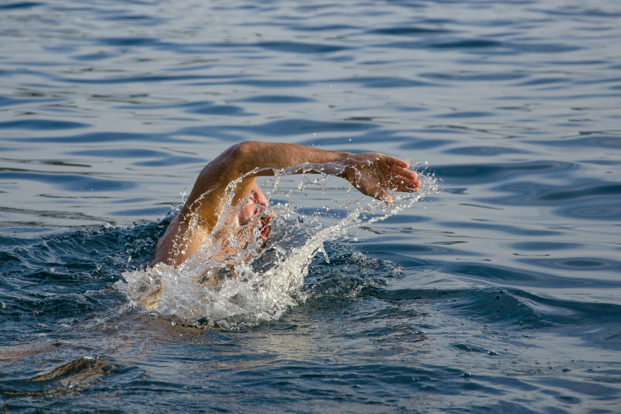 A male swimmer performing freestyle stroke in open water, creating splashes.