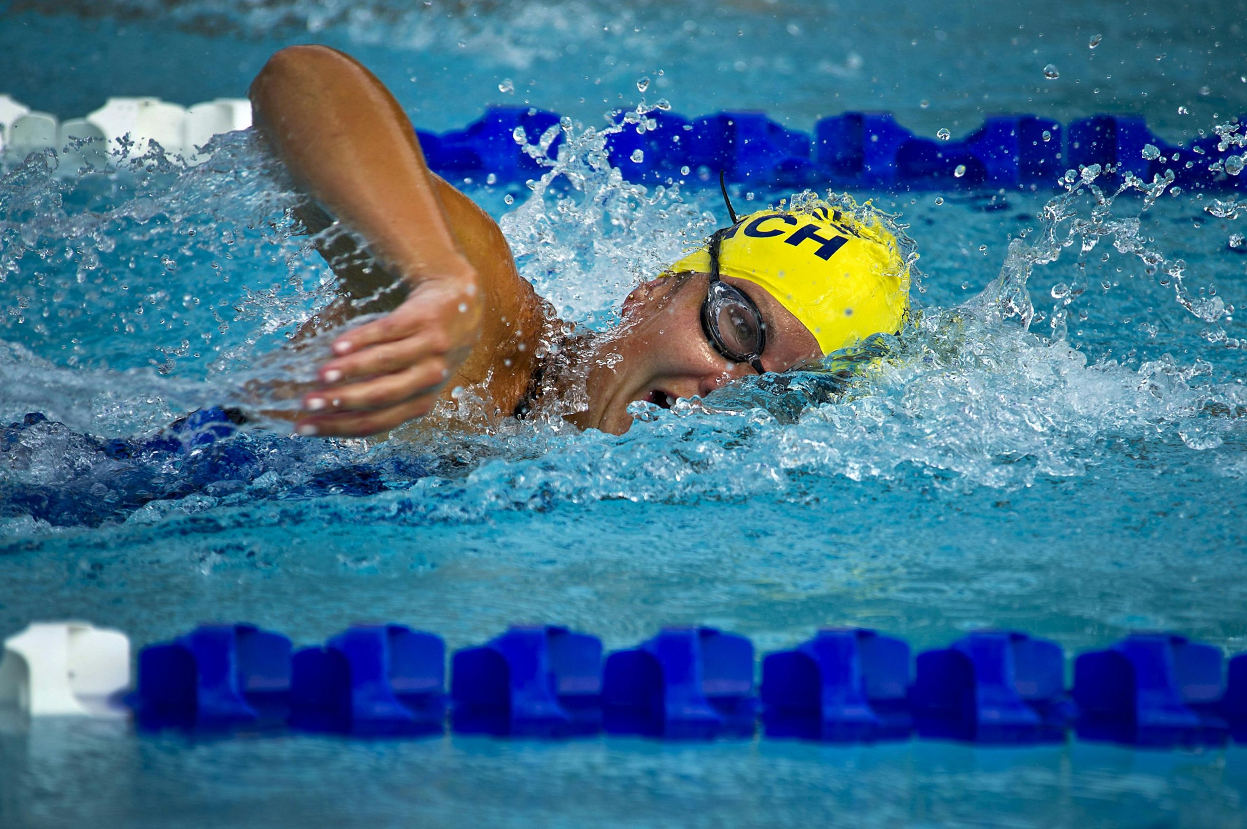 Swimmer wearing a yellow cap and goggles competing in a swimming pool